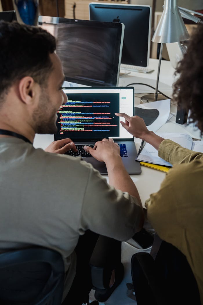 gallery-5 Two programmers working together on a laptop, discussing code in a modern office setting.